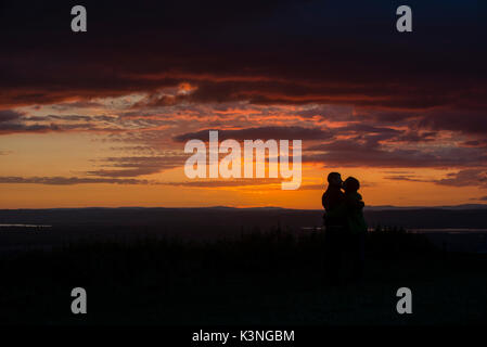 A couple kiss as they watch the sunset from Coaley Peak in Gloucestershire. Stock Photo