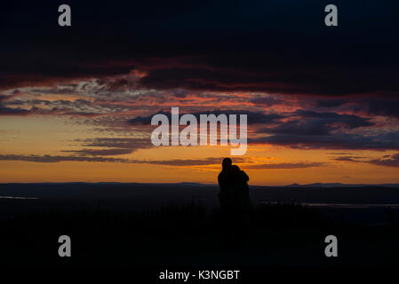A couple cuddle as they watch the sunset from Coaley Peak in Gloucestershire. Stock Photo