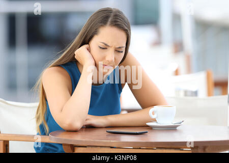 Single sad woman waiting for a mobile phone message or call sitting in a coffee shop