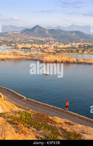 Tourist on a road admires the sail boat in the clear sea around the village of Ile Rousse Balagne Region Corsica France Europe Stock Photo