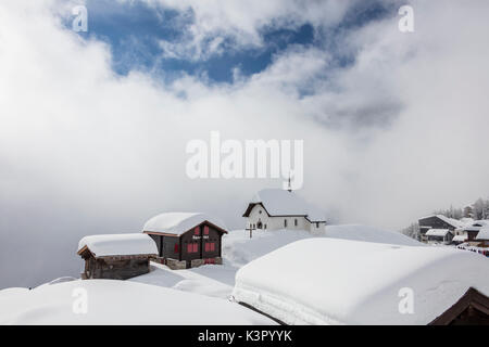 Blue sky and clouds frame the mountain huts covered with snow Bettmeralp district of Raron canton of Valais Switzerland Europe Stock Photo