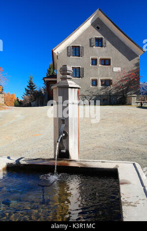 Typical house of low Engadine in front of a fountain in the village of Bos-Cha Switzerland Europe Stock Photo
