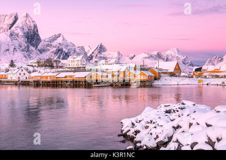 The colors of dawn frames the fishermen houses surrounded by snowy peaks Sakrisøy Reine Nordland Lofoten Islands Norway Europe Stock Photo