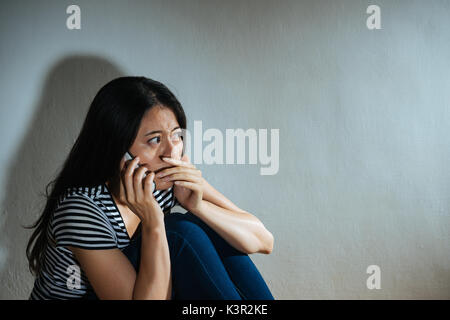 battered abused women concept - closeup photo of fear sadness woman having family violence problem using mobile cellphone calling police help in dark  Stock Photo