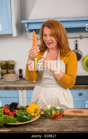 Housewife in the kitchen holding huge carrot. Stock Photo