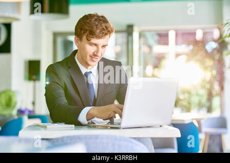 Portrait of handsome successful businessman working at desk using laptop while doing internet research and marketing analysis Stock Photo
