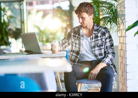 Portrait of pensive young man sitting at table in cafe using laptop Stock Photo