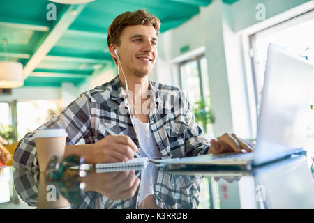 Portrait of smiling young man dressed in casual clothes using video chat while working with laptop in modern office Stock Photo