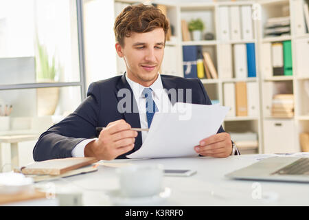 Portrait of successful young businessman working at desk in modern office, reading documents Stock Photo