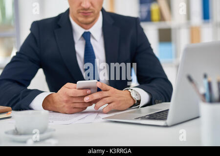 Mid section of unrecognizable young businessman using smartphone at desk in office Stock Photo