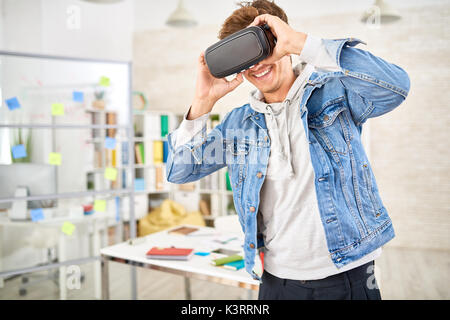 Portrait of young man enjoying video in VR glasses smiling standing in modern office space Stock Photo