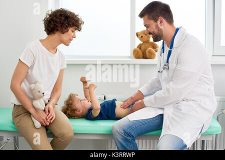 Portrait of smiling doctor examining stomach of little boy and asking him to say where it hurts Stock Photo