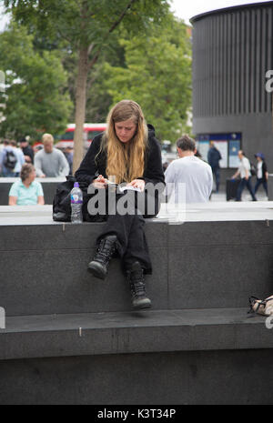 Woman reading in sitting on a stone bench in the street, in London, United Kingdom Stock Photo