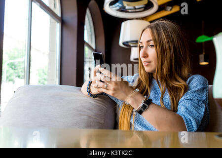 Portret of young female reading sms on the phone in cafe. Toned. Selective focus. Stock Photo