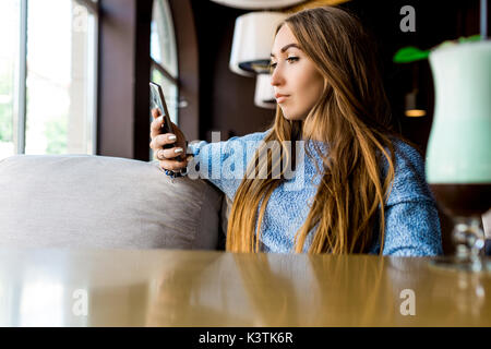 Portret of young female reading sms on the phone in cafe. Toned. Selective focus. Stock Photo