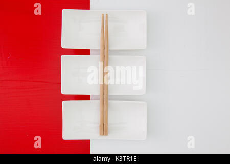 Empty ceramic bowls and bamboo chopsticks for sushi food on the red and white wooden table Stock Photo