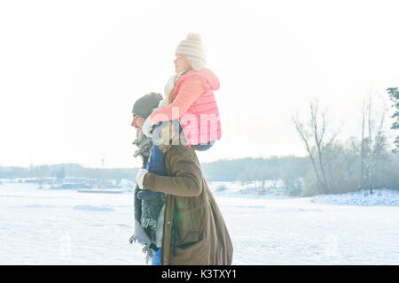 Father with child in winter giving her a piggyback ride Stock Photo