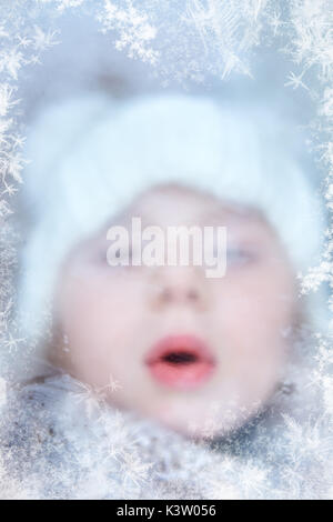 Child in winter blows on iced window with frost pattern Stock Photo