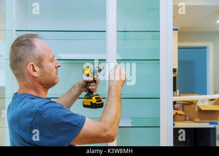 Construction worker sets a new handle a screwdriver installing kitchen cabinets Stock Photo