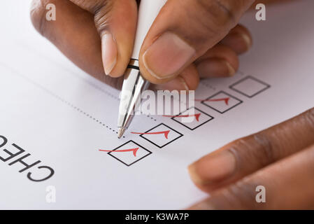 Close-up Of Person's Hand Marking On Checklist Form With Red Pen Stock Photo