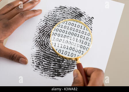 Close-up Of Person Using Magnifying Glass To Check Binary Code Within Finger Print Stock Photo