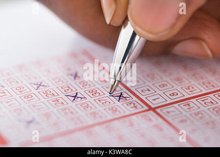 Close-up Of Person's Hand Marking Number On Lottery Ticket With Pen Stock Photo