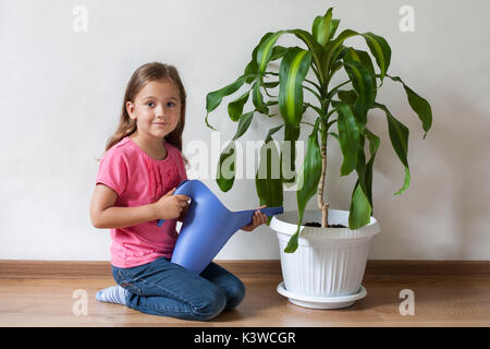 Cute Little Six-year Girl Child Watering From Watering Can In Her Hand Plant Palm Blue Watering Can Indoor. Care For Plants. Stock Photo