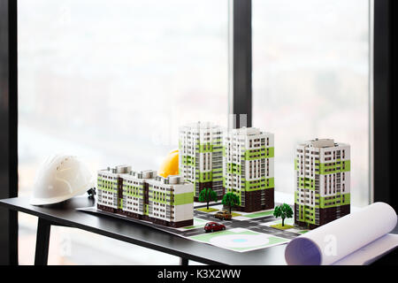 Model of residential quarter and hardhats on table in office Stock Photo