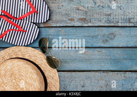 Still life of different items for relaxing on the beach, rubber flip-flops, hat, camera, phone, sunglasses, headset on a wooden blue background. Conce Stock Photo