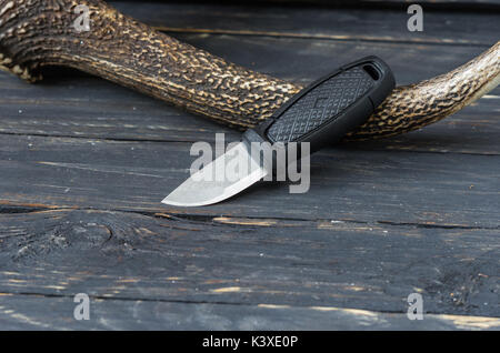 Small tourist knife on a black wooden background with a reindeer horn. Tourist accessories Stock Photo