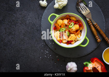 Vegetable stew of cauliflower, carrots and tomatoes on a black background. Stock Photo