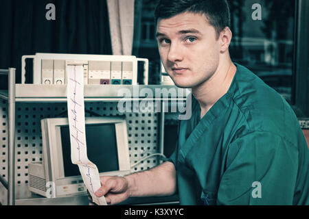 Male doctor in uniform is holding analysis of electrocardiograph examination while sitting in the hospital ward. Healthcare concept Stock Photo