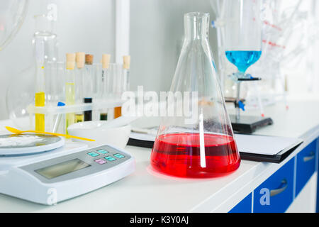 White powder on special scales near fask with red liquid for some research in a laboratory. Healthcare and biotechnology concept Stock Photo