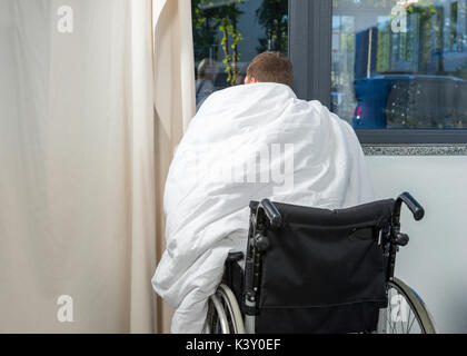 Ill patient sitting by the window on wheelchair covered with quilt in hospital ward. Healthcare concept Stock Photo