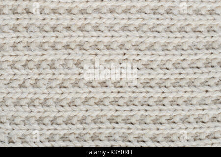 The texture of a thick knitted sweater beige close-up. Uniform knitting pattern Stock Photo