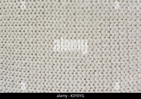 The texture of a thick knitted sweater beige close-up. Uniform knitting pattern Stock Photo