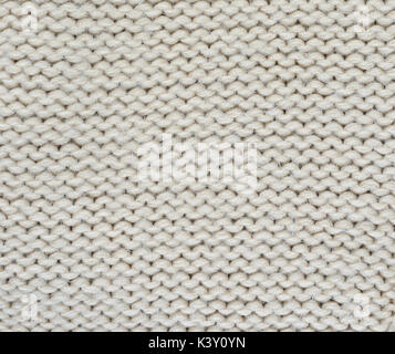 The texture of a thick knitted sweater beige close-up. Uniform knitting pattern Stock Photo
