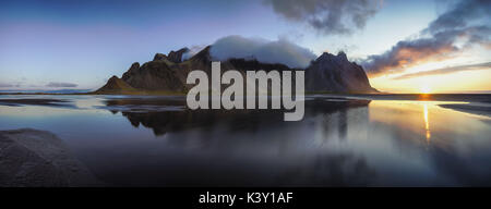 Panoramic view of Vestrahorn mountain reflected in shallow water at sunrise. Stock Photo