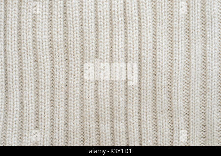 Texture of a beige knitted sweater close-up. Vertically oriented pigtails on knitted fabric. Uniform knitting pattern Stock Photo