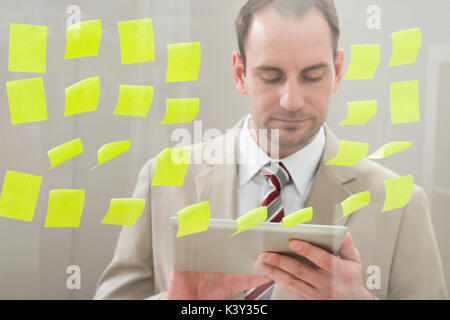 Businessman Using Digital Tablet In Front Of Adhesive Notes On Glass Wall Stock Photo