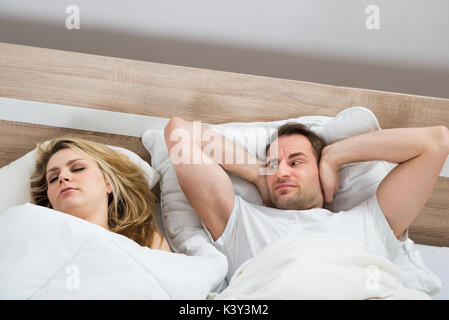 Man Covering Ears While Woman Sleeping In Bedroom At Home Stock Photo