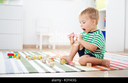 two years old child sitting on the floor with wooden cubes Stock Photo