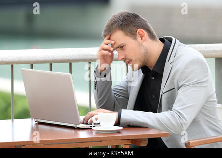 Single worried businessman reading bad news on line with a laptop sitting in a bar Stock Photo