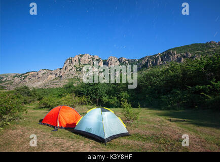 Tourist tents in a clearing in the mountains against the starry sky and the mountain peak Stock Photo