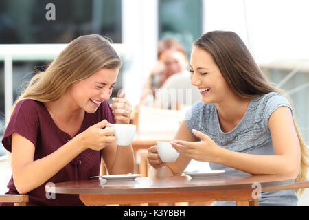 Two best friends laughing loud during a conversation sitting in a restaurant