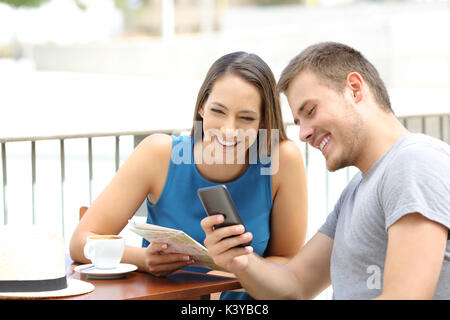 Couple of tourists searching on line locations in a smart phone and guide during travel sitting in a coffee shop Stock Photo