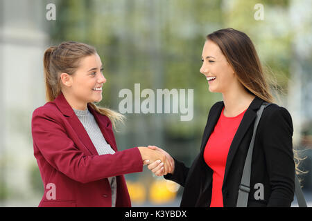 Side view of two happy executives meeting and handshaking on the street Stock Photo