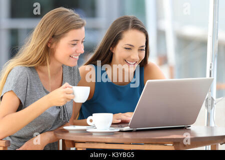 Two funny friends watching media content in a laptop sitting in a bar Stock Photo