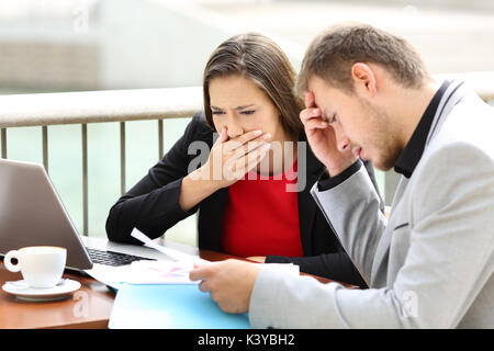 Two worried executives reading documetns complaining after discover a mistake sitting in a bar Stock Photo