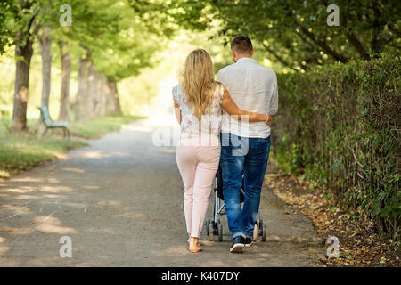Mother, father and baby in a stroller walk in the park. Stock Photo